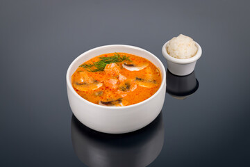 Tom Yam soup with salmon on black with reflection