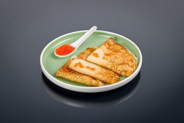 pancakes with red caviar on a green plate on black with reflection