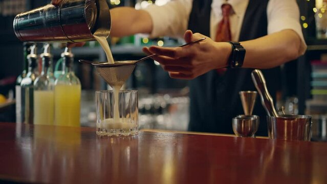 4K Professional male bartender preparing and serving cocktail drink to customer on bar counter at luxury nightclub. Barman making mixed alcoholic drink for celebrating holiday party at restaurant bar.