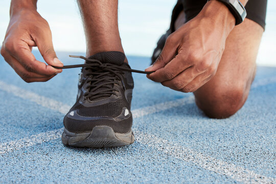 Active athletic man preparing for a practice run to increase stamina for a competitive race on an Olympic track. Closeup of a fit african american athlete tying his shoelaces before running outside.