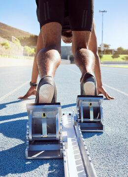 Feet of athlete in starting position on a running track. A male track and field runner ready to leave the starting block to start his sprint. Sportsman with hands on the starting line during a race