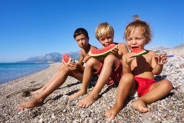 Two brothers eat a watermelon on the beach