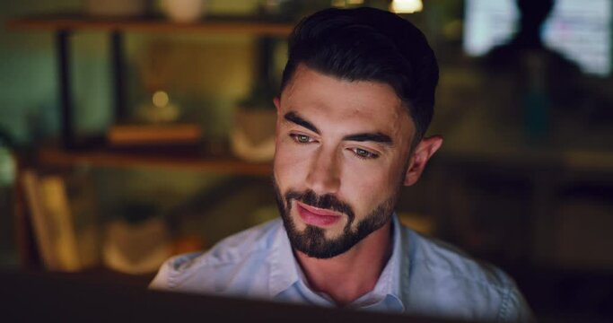 Young business man working late on a computer in an office at night. Face of a hardworking entrepreneur reading emails, doing research online and compiling reports while planning ideas for deadlines