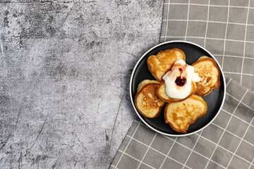 Fluffy buttermilk pancakes with berry jam on a round plate on a dark gray background. Top view, flat lay