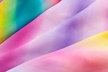 Background of silk fabric in iridescent shades. Texture background of silk fabric folded in the form of folds. Multi-colored silk is folded diagonally.