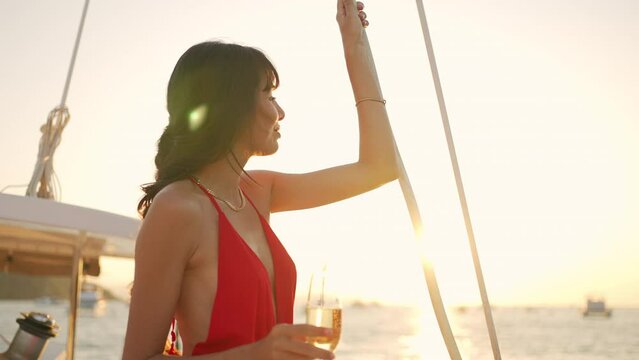 4K Attractive Latin woman enjoy luxury outdoor lifestyle drinking champagne while catamaran boat sailing in the sea at summer sunset. Beautiful female relaxing on sail yacht on holiday travel vacation