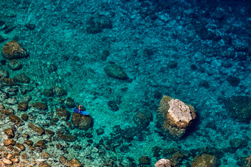 Aerial view of an unrecognizable adult man on a blue SUP Stand Up Paddling board paddling along the rocky coastline with clear water of the bay Cala en Basset at Mallorca with copy space at the top.