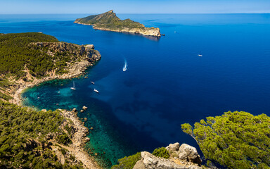 Panorama view from a cliff of the rocky coastline of idyllic Mallorca cove Cala en Basset nearby Sant Elm with boats and the island Sa Dragonera with the mountain Puig des Aucells in the background.