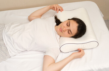 A woman sleeps on an orthopedic pillow made of memory foam, lying on a bed. The correct pillow for...
