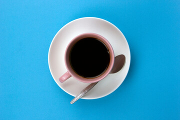 An isolated black coffee on light pink cub on blue background with small spoon