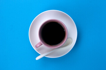 An isolated black coffee on light pink cub on blue background with white spoon