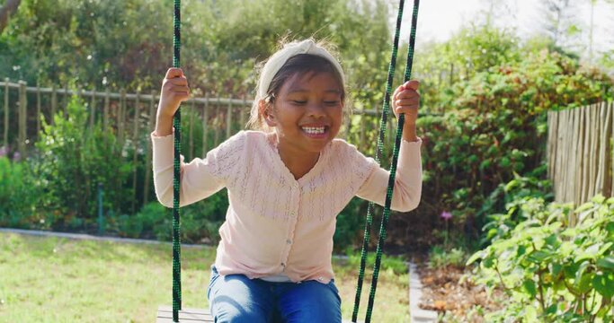 One adorable little girl playing on a swing in the backyard at home on a sunny day. A cute child having fun and smiling at a park during summer. Happy, playful and active girl enjoying her childhood