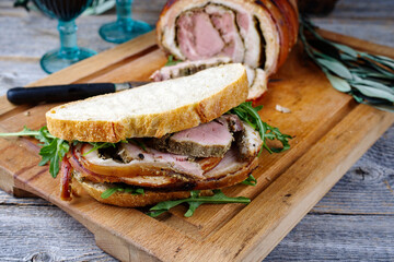 Traditional barbecue Italian porchetta pork belly roll meat sandwich with rocket salad served as...