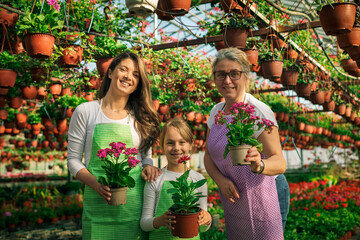 Grandmother, mother and daughter posing for photo while holding flowers in greenhouse.