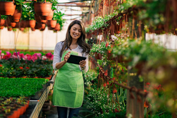 A small business owner uses a tablet while checking flowers for delivery in a greenhouse.