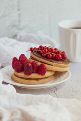 Round cakes with fresh red berries, a white ceramic mug with herbal tea on a light background. Cozy composition of a delicious breakfast in bright colors