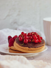 Round cakes with fresh red berries, a white ceramic mug with herbal tea on a light background. Cozy composition of a delicious breakfast in bright colors