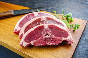 Raw lamb saddle back chop steak with herbs offered as close-up on a wooden design board