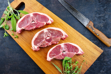 Raw lamb saddle back chop steak with herbs offered as top view on a wooden design board