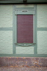 Fenster mit braunen heruntergezogenen Rolläden an einer grünen Hauswand mit Fachwerkbalken,...