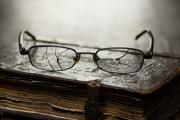 Glasses with cracked glasses on an antique book in a leather antique binding, studio shot.