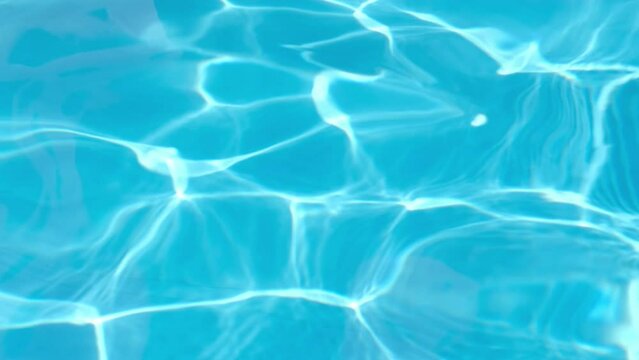 Background of pure light blue water in swimming pool with sun reflections. Rippled water surface in pool