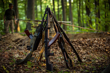 five AK-74 Kalashnikov assault rifles stand together on the ground in the forest with their muzzles...