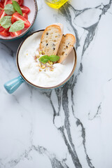 Turquoise bowl with stracciatella di bufala, tomatoes and ciabatta. Top view on a black and white marble background, vertical shot with space