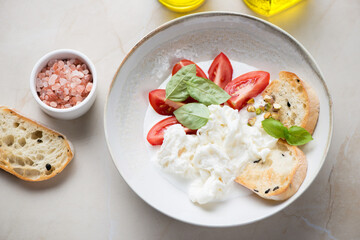Plate of stracciatella or stretched curd cheese served with tomatoes, ciabatta and fresh basil,...