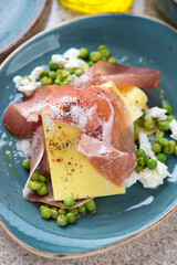 Close-up of open lasagna with prosciutto, ricotta and crushed green peas served on a turquoise plate, vertical shot