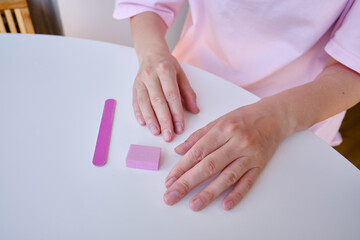 The girl files her nails with a pink nail file making a manicure. Spa nail care. Well-groomed hands after manicure. Hand hygiene
