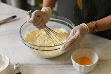 A hands in rubber gloves stirring 
dough for a cake  