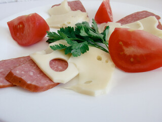 Still life. Sliced tomatoes, cheese sausage salami on a white plate. Light background.