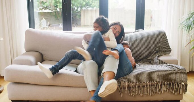 Happy family having fun on a sofa at home. Young single mother being playful while bonding with her two daughters on couch in the living room. Little girls love having their mom around on a weekend