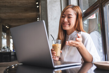 A beautiful young asian woman using laptop computer for video call, online meeting while drinking coffee