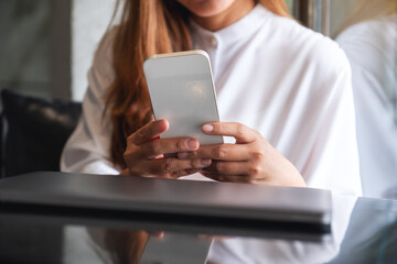 Closeup image of a woman holding and using smart phone with laptop computer on the table