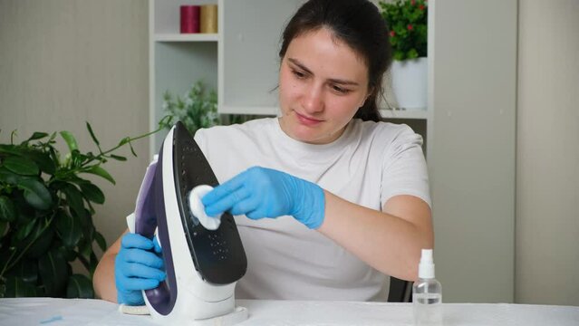 The housewife sprays a special solution on the dirty sole of the iron.