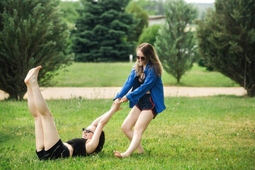 Fototapeta premium two beautiful sports girls have fun and pose in the summer in nature, dressed in swimwear and sportswear on a bright green meadow, active youth spend leisure time in the hot season