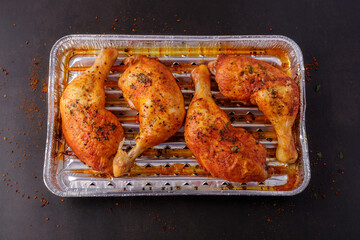Marinated in tomato sauce with herbs and pepper baked grilled legs of chicken in disposable...