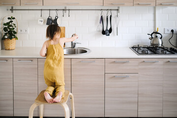 Funny baby washes his hands in bright real kitchen