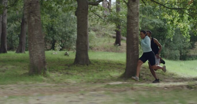 Fit couple running fast outdoors in a forest for their morning exercise routine. Active athletic friends sprinting together in nature on a summer day. Two people doing fitness and cardio training