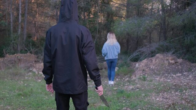 A man with a knife in the forest. The maniac pursues the victim and prepares to attack. The girl runs away from the killer
