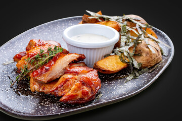 Chicken in Teriyaki sauce with roasted potatoes.In peel and garlic sauce. On a dark background, isolated.