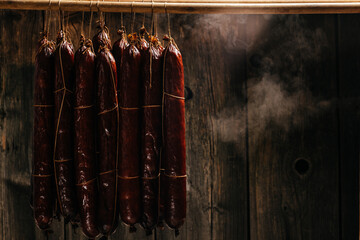 Fototapeta na wymiar The process of smoking hanging sausages in the smokehouse. Clouds of smoke rise up and envelop the sausages hanging in a row. Long banner format