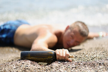 Drunk man lying on seashore with bottle of wine in hand