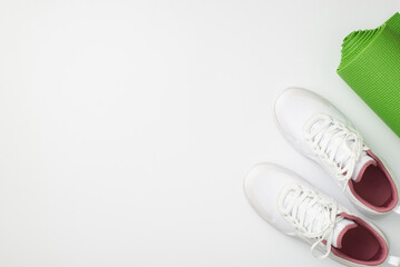 Active lifestyle concept. Top view photo of white sneakers and green sports mat on isolated white background with copyspace
