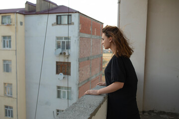 A depressed young girl stands on the balcony and looking away