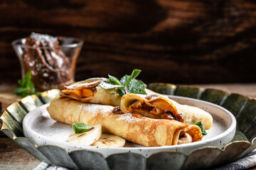 Crepes stuffed with chocolate spread and banana on white plate. Thin pancakes, blini. Delicious breakfast or snack. Food recipe background. Close up