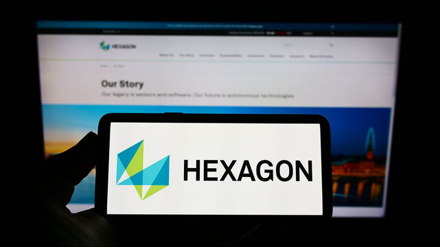 Stuttgart, Germany - 01-16-2022: Person holding mobile phone with logo of Swedish software company Hexagon AB on screen in front of business web page. Focus on phone display.