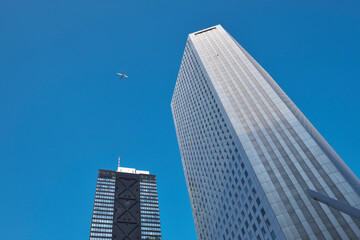 Fototapeta na wymiar 雲一つ無い青空が背景の新宿超高層ビル群と、上空を飛ぶ羽田新ルートのジェット機